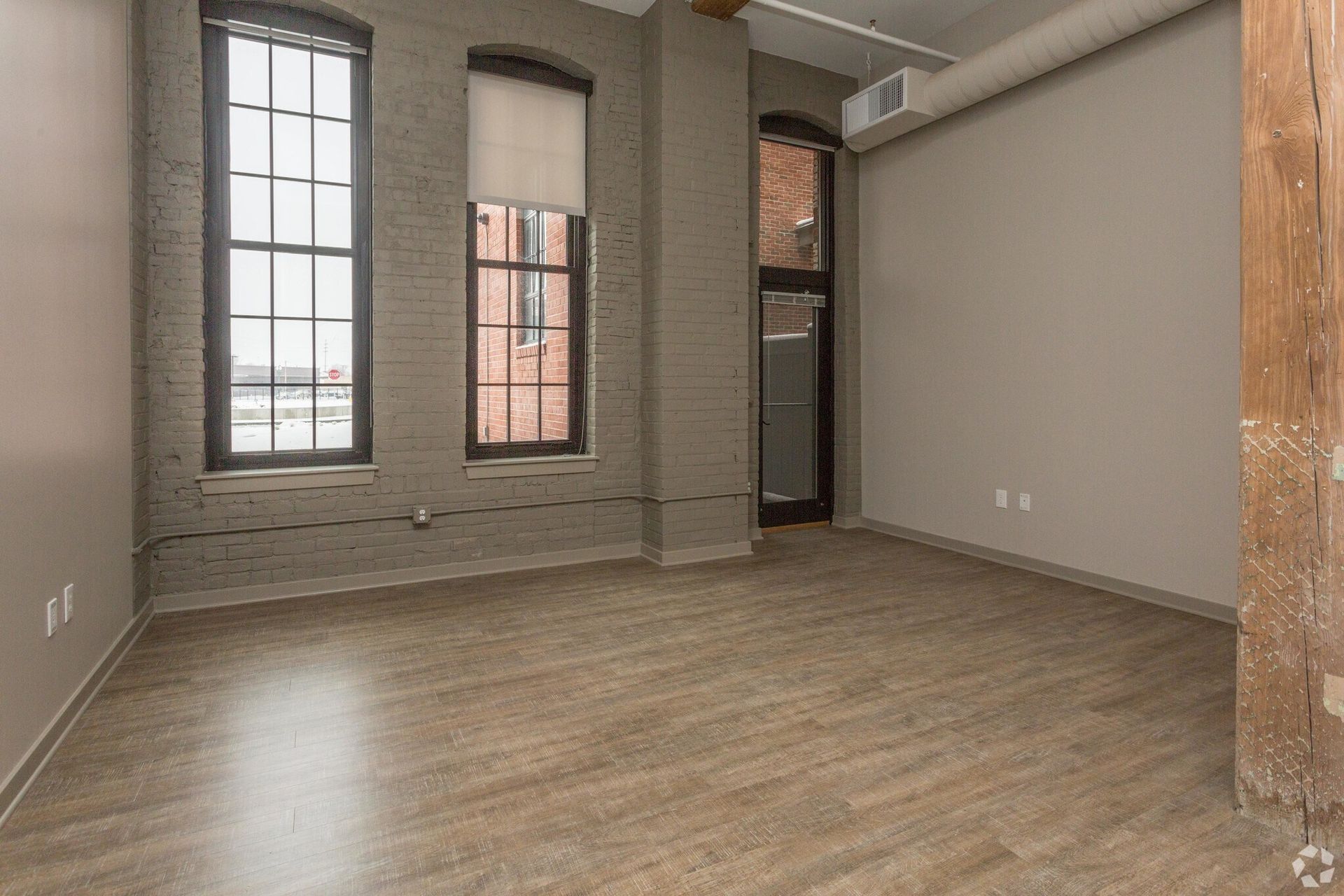Empty room with large windows, brick columns, and wood floors.