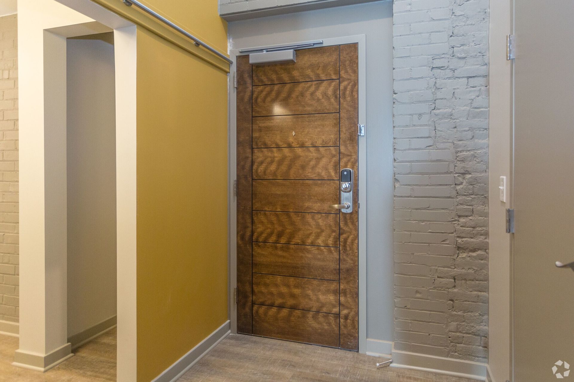 Wooden door with a modern lock in a building hallway, brick wall on one side.