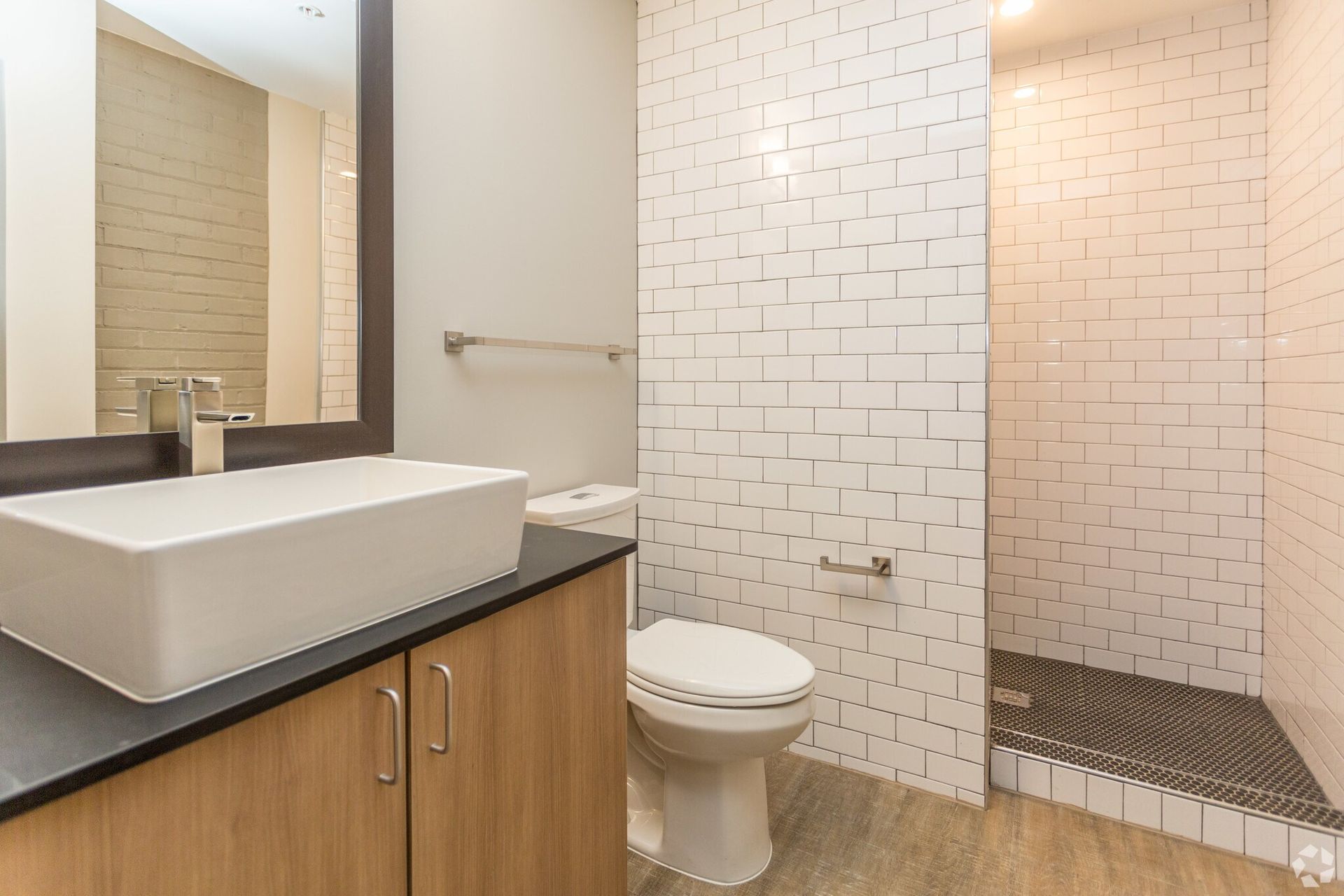 Modern bathroom with white rectangular sink, toilet, and tiled shower. Light wood cabinet and floor.