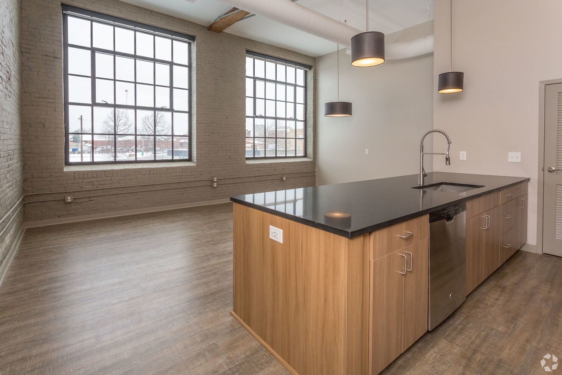 Modern kitchen with wood cabinets, black countertop island, and large industrial windows.