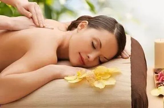 Una donna riceve un massaggio alla schiena con dei fiori gialli accanto a lei in un ambiente termale.