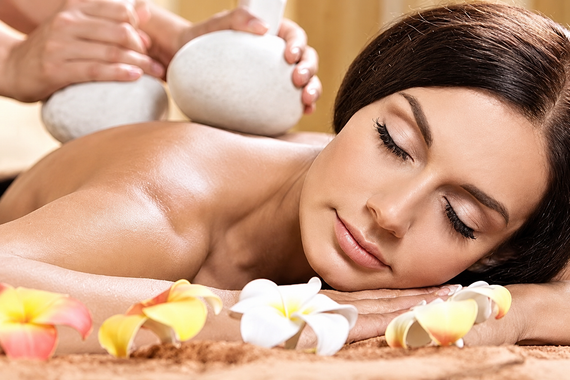 Una donna si rilassa durante un massaggio in una spa, con candele e petali di fiori nelle vicinanze.