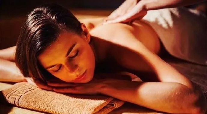 Persona che riceve un massaggio su un asciugamano, con gli occhi chiusi, in un ambiente termale riscaldato.