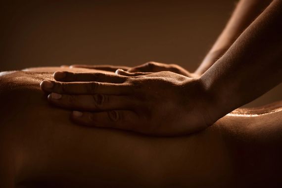 Donna sdraiata su un fianco durante un massaggio in una spa, con uno scrub caldo e dorato sulla schiena e sulle spalle.