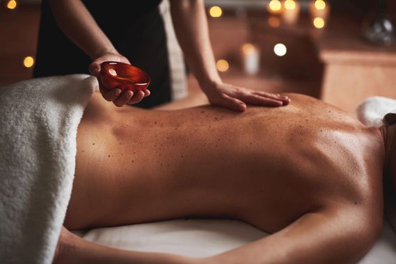 Una donna riceve un massaggio alle spalle su un lettino da spa, con un fiore bianco tra i capelli.