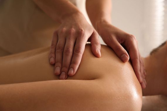 Una donna riceve un massaggio alle spalle su un lettino da spa, con un fiore bianco tra i capelli.