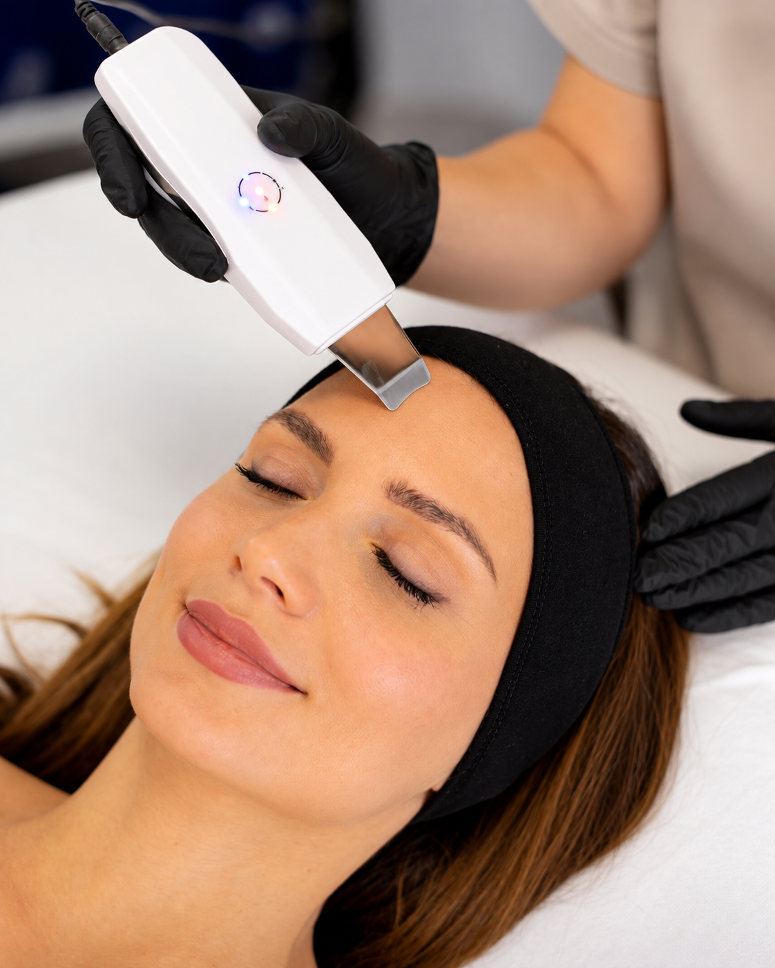 Dispositivo per trattamenti viso che scorre sulla fronte di una cliente rilassata in una spa