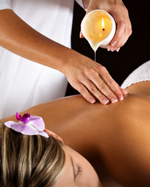 Olio di candela versato sulla schiena di una persona durante un massaggio in una spa, con candele accese sullo sfondo.