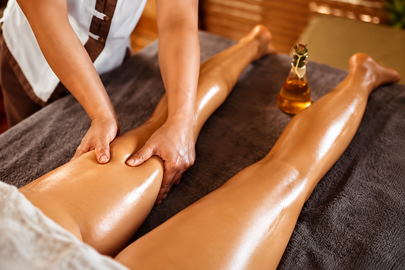 Una massaggiatrice massaggia le gambe unte d'olio su un lettino da spa, con una bottiglia di olio da massaggio nelle vicinanze.