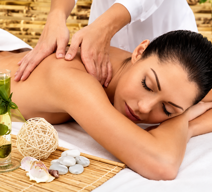 Massaggio spa con una donna sdraiata a pancia in giù mentre delle mani le massaggiano le spalle, vicino ad asciugamani bianchi e decorazioni
