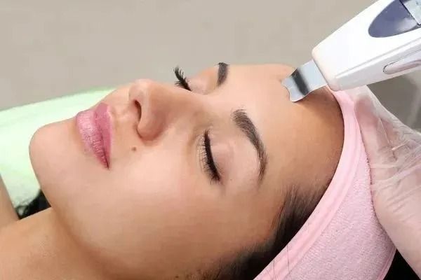 Una donna, sdraiata su un lettino da trattamento, riceve un trattamento viso con un dispositivo portatile sulla fronte.