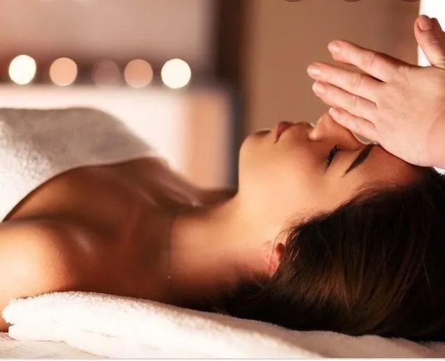Una donna riceve un massaggio al viso in una spa, sdraiata su un asciugamano mentre delle mani le accarezzano delicatamente il viso.