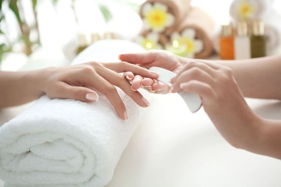 Mani che ricevono una manicure su un asciugamano bianco, con luci soffuse da spa e fiori sullo sfondo.