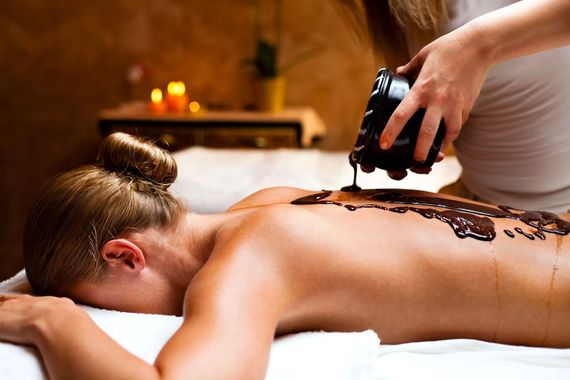 Una persona riceve un massaggio con pietre calde su un lettino da spa, con candele accese sullo sfondo.