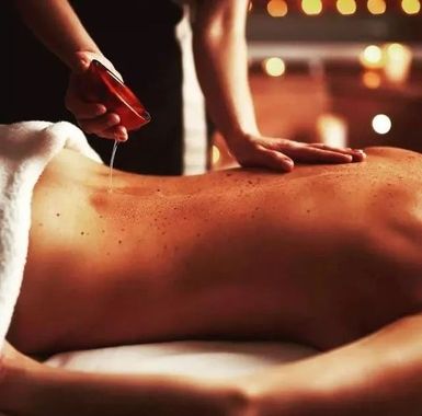 Massaggiatrice che applica olio sulla schiena di un cliente in una sala spa illuminata da luci soffuse.