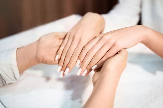 Mani con unghie curate appoggiate insieme su un asciugamano bianco da spa.