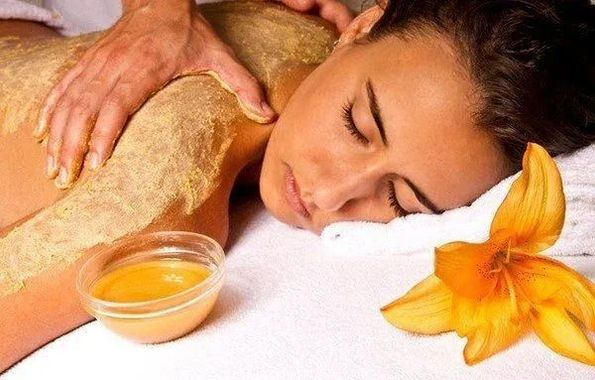 Persona che riceve un massaggio in una spa con un fiore e una ciotola d'olio su un asciugamano bianco.