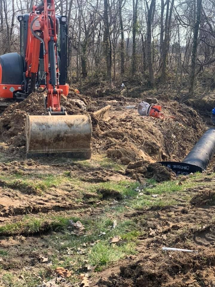 Orange excavator digging in a muddy yard; black pipe nearby. Trees in the background.