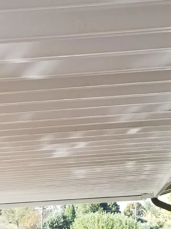 White corrugated awning with dappled sunlight, trees visible below.