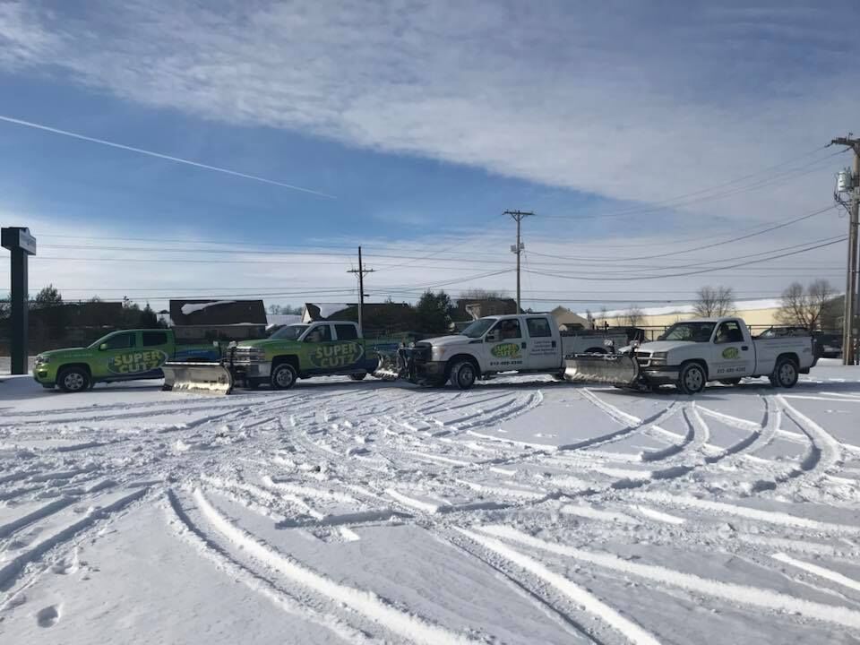 Four service trucks parked in a snowy lot on a sunny day.