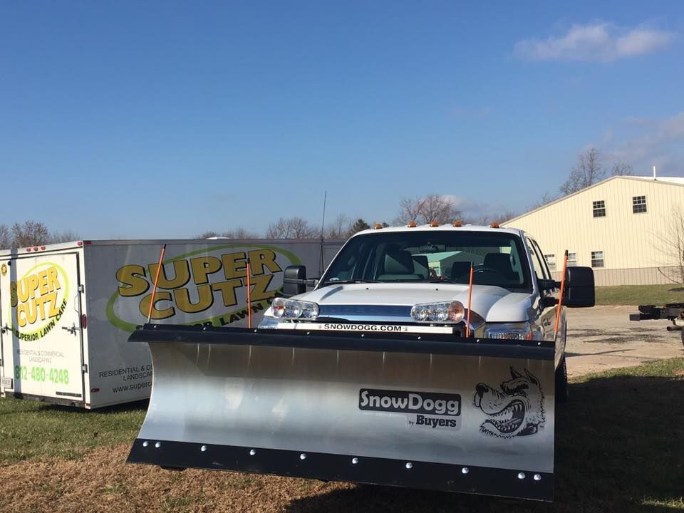 White truck with snow plow; parked next to a trailer with 
