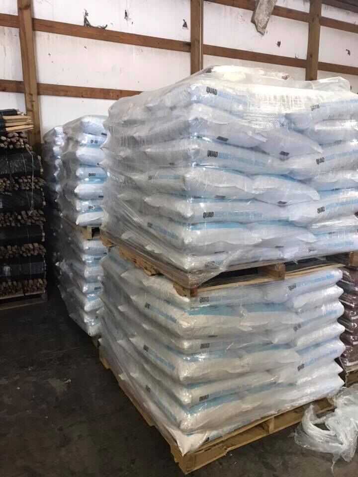 Pallets stacked with bagged goods, wrapped in clear plastic, inside a warehouse.