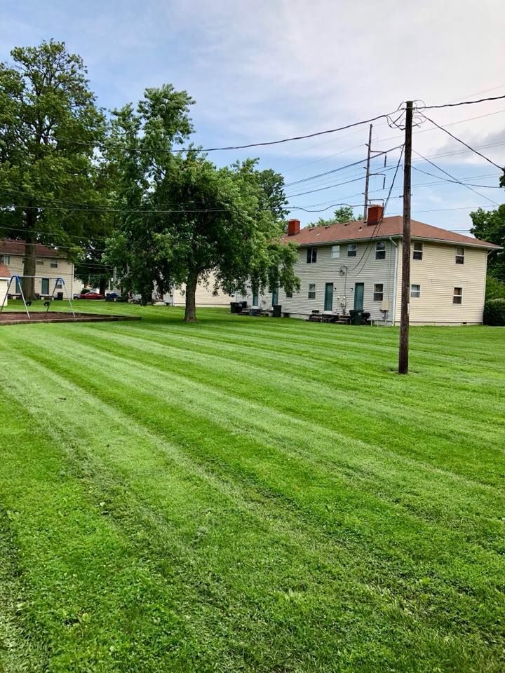 Lush green lawn with freshly cut stripes, two-story beige apartments in the background, trees, and power lines.