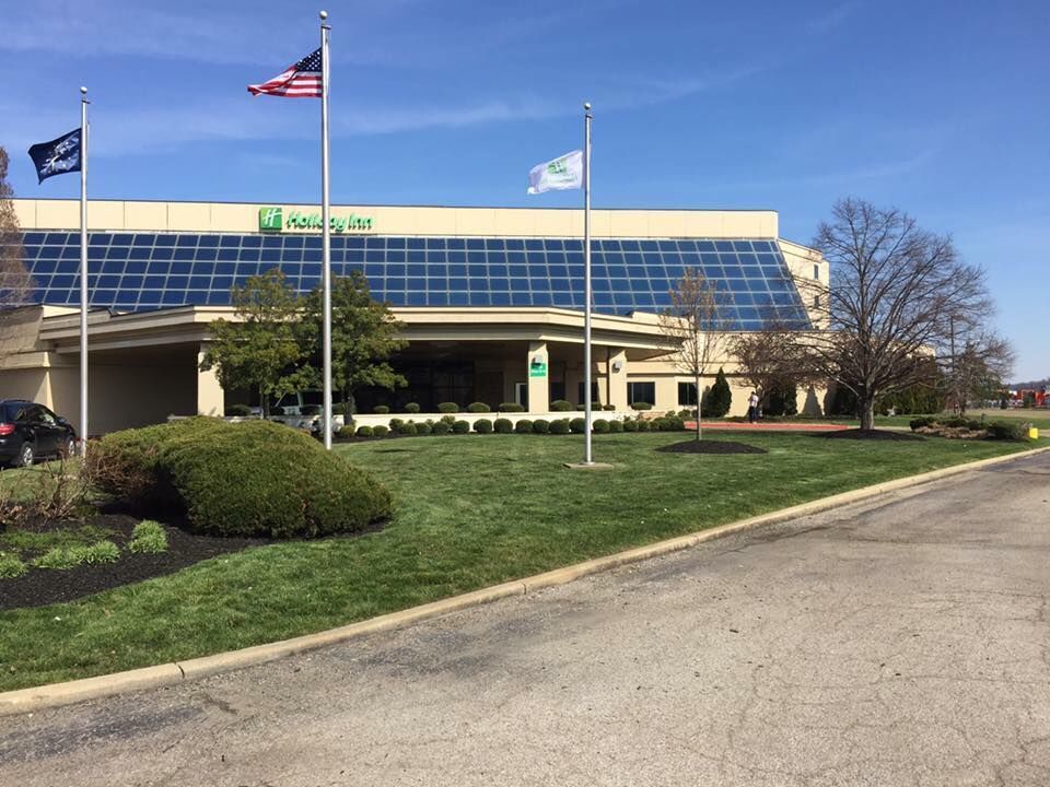 Holiday Inn hotel with flags on a sunny day. Green grass and shrubbery in front.