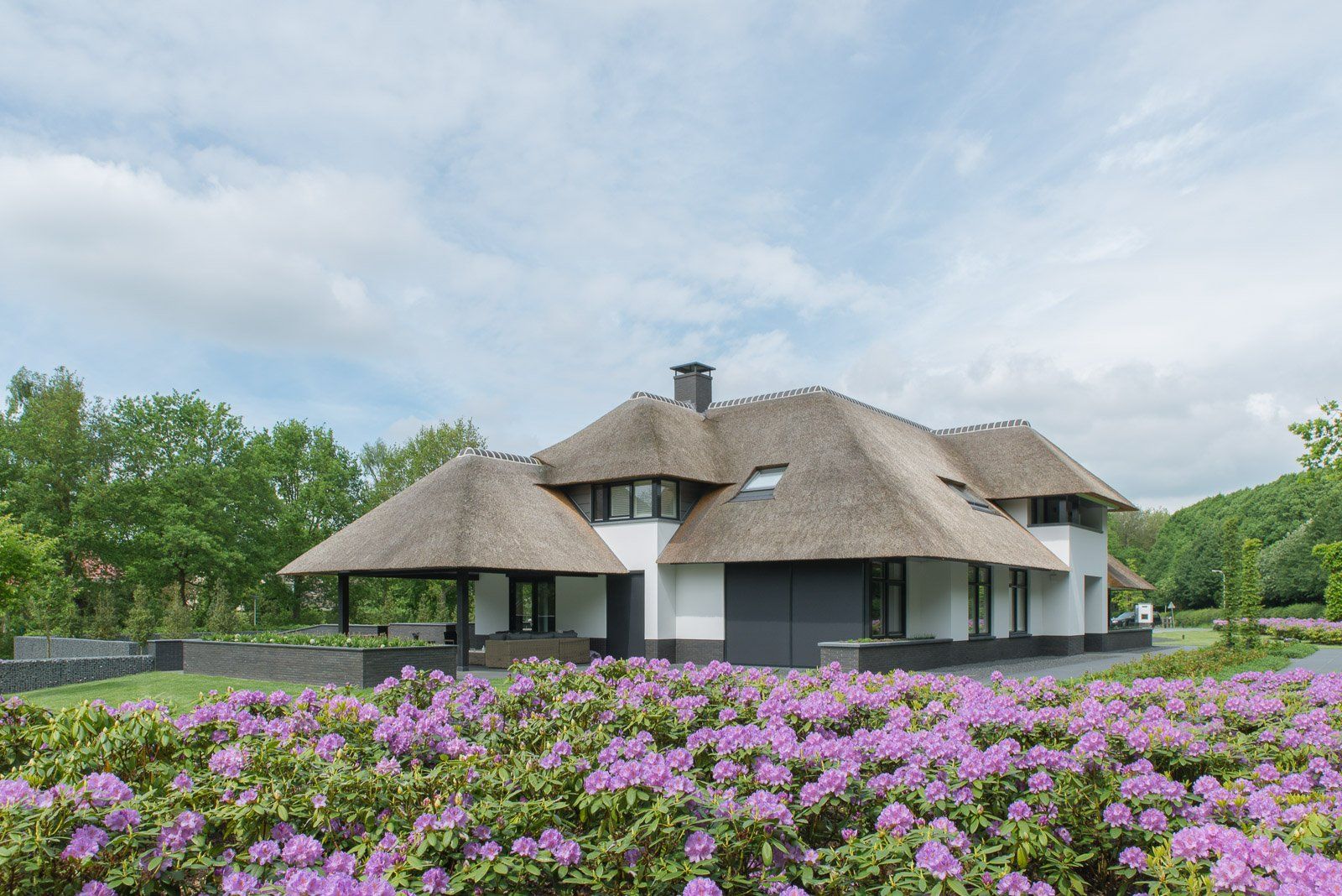 Modern wit huis met rieten dak en paarse bloeiende struiken ervoor.