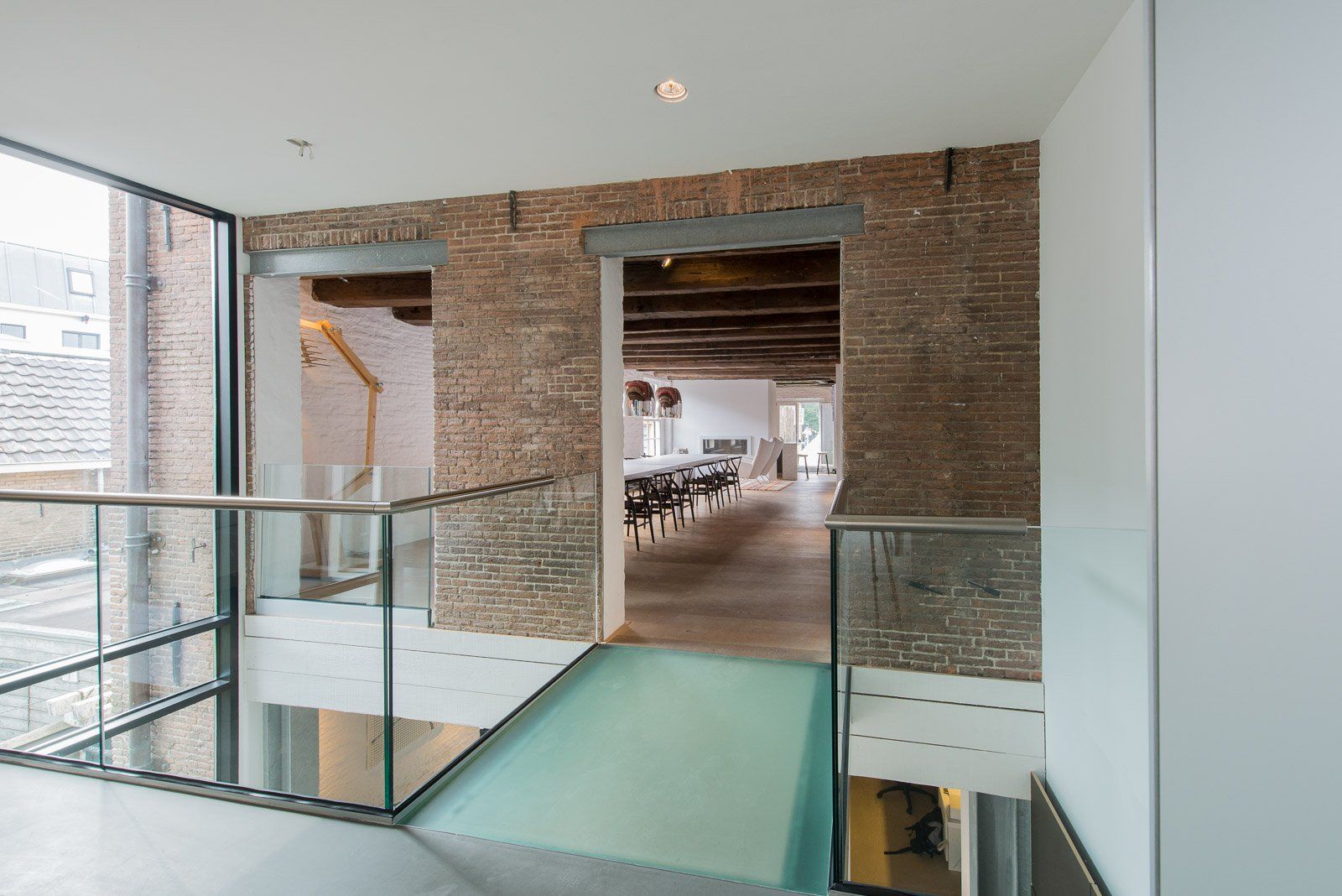 Binnenhal met glazen balustrade en bakstenen bogen die toegang geven tot de eetkamer.