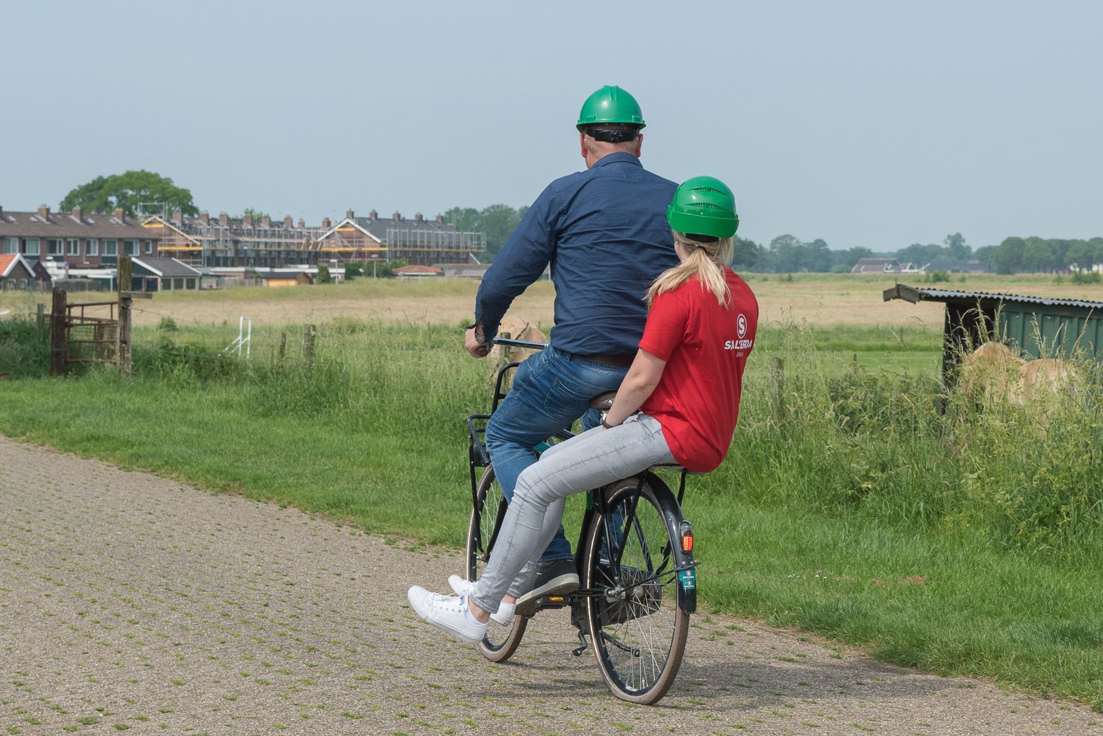 Een man en een vrouw fietsen over een pad, beiden dragen een groene helm.