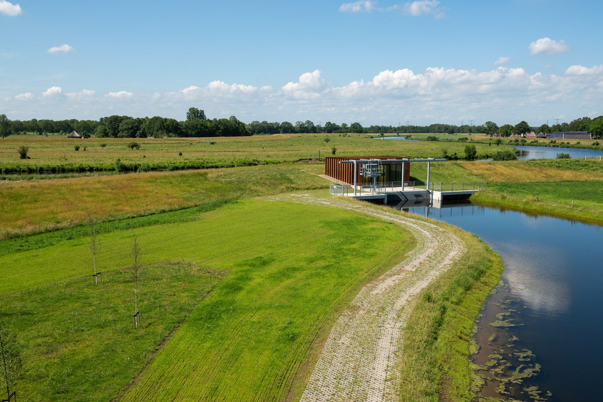 Een moderne hut op een steiger, naast een waterweg en een grasveld onder een blauwe hemel.
