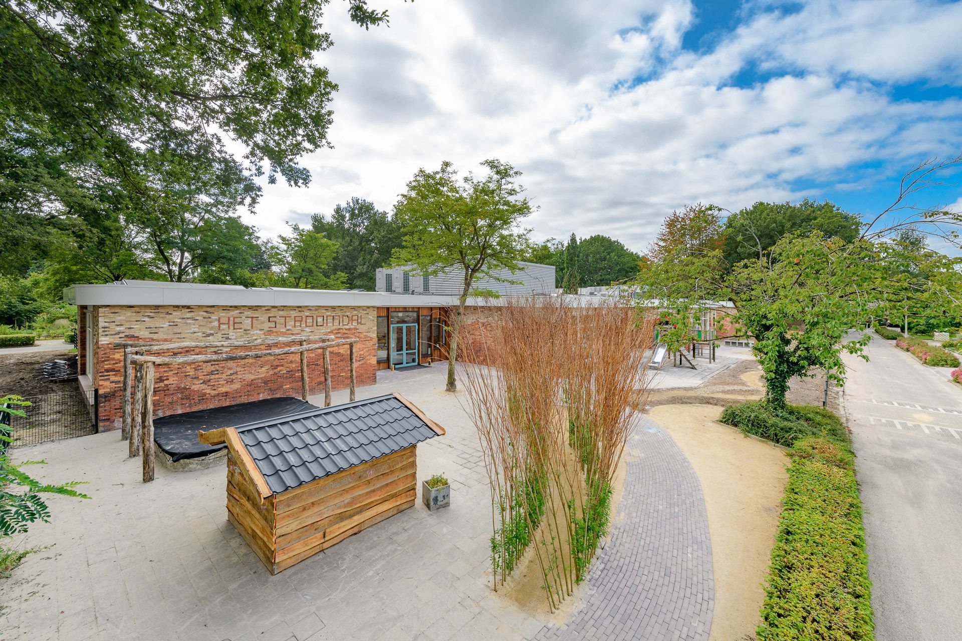 Binnenplaats met houten constructies, aangelegde tuinen en een bakstenen gebouw onder een bewolkte hemel.