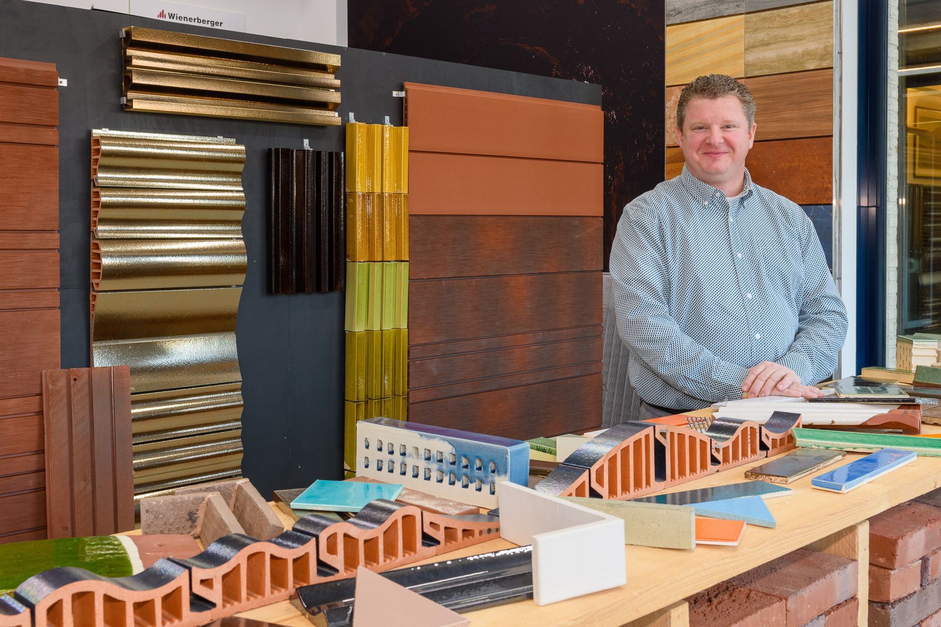 Een man staat achter een display met bouwmaterialen in verschillende kleuren en texturen.