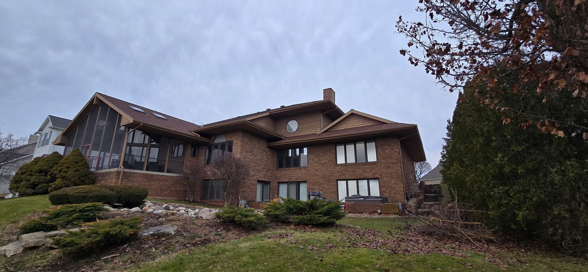 Brick house on a sloped, wooded lot under a cloudy sky