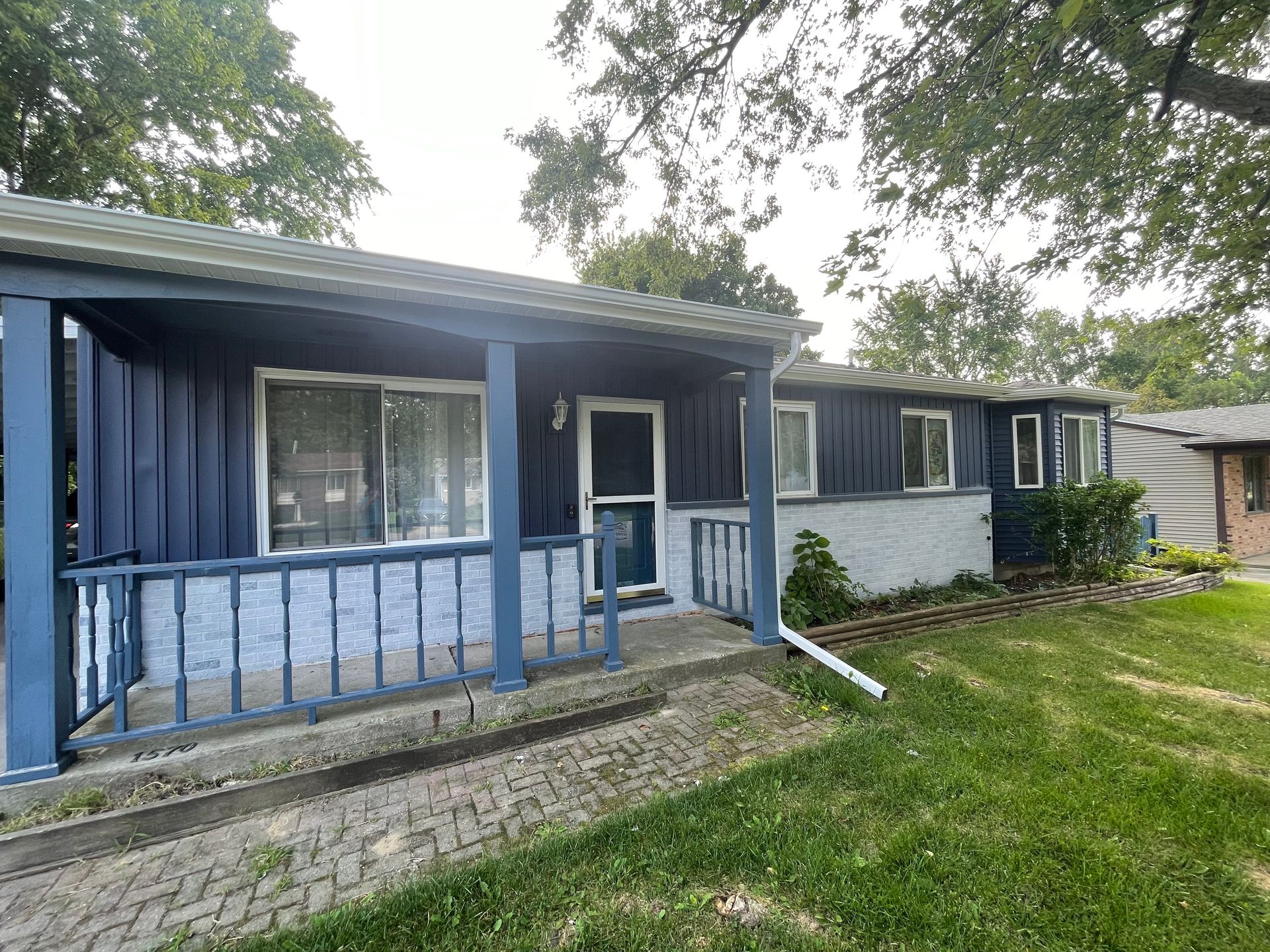 Blue single-story house with a front porch, railing, and a ramp leading to the entrance.
