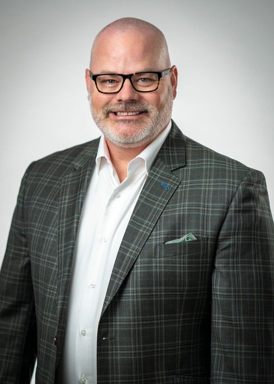 Smiling bald man in glasses wearing a gray plaid blazer and white shirt against a light gray background