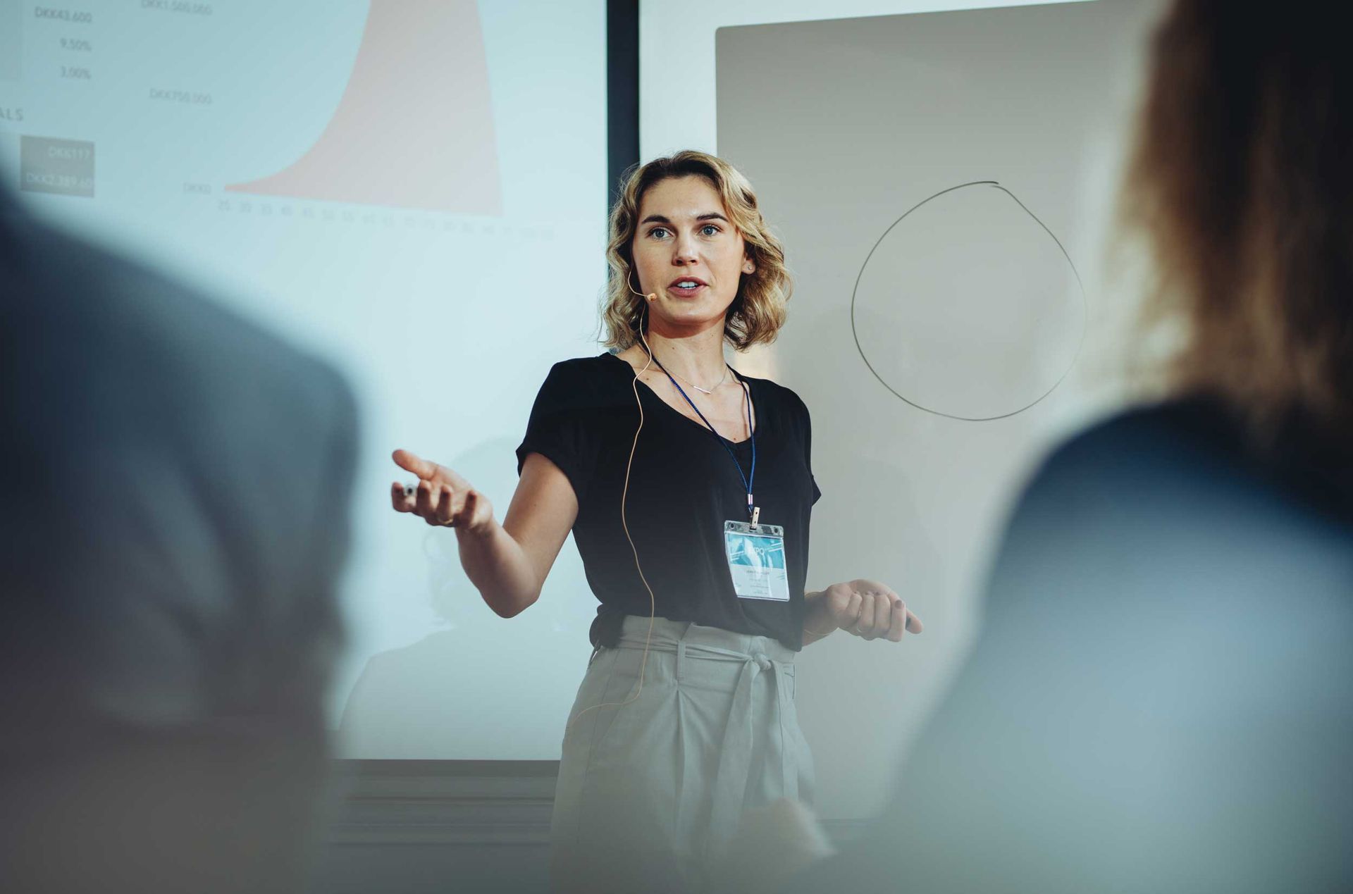 Presenter speaking in front of a projected slide, gesturing during a meeting
