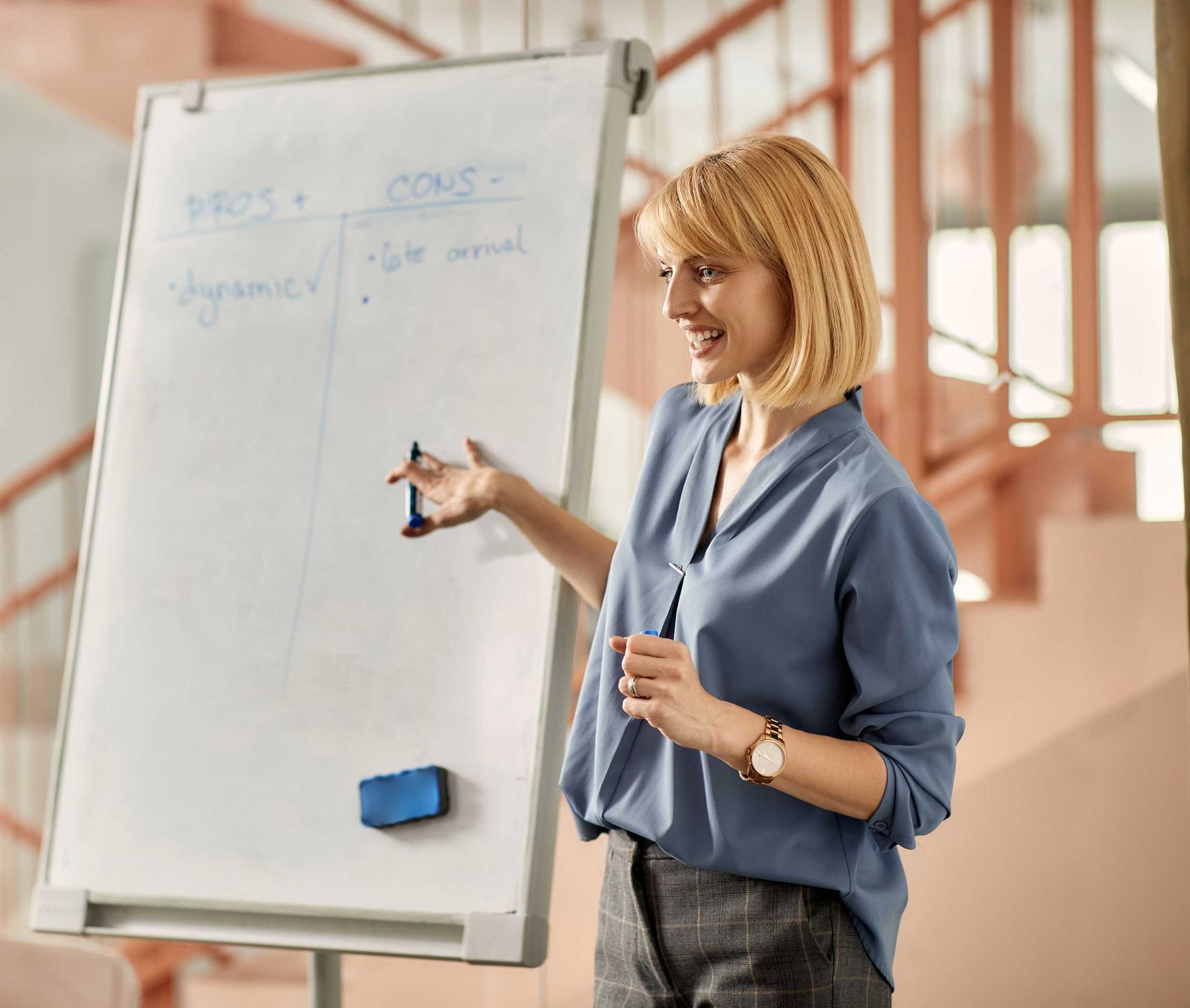 Woman presenting at a flip chart in a bright office, pointing to notes with a marker.