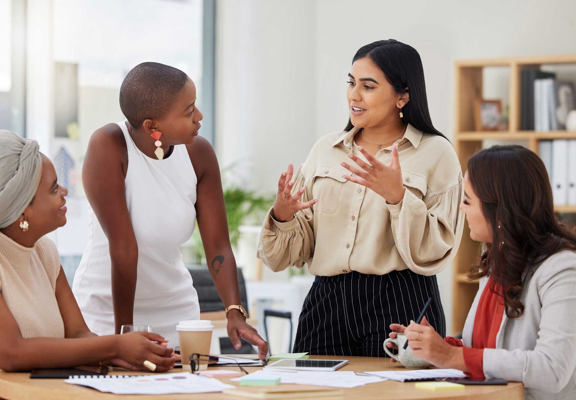 Team meeting around a table, with one woman speaking while others listen and take notes