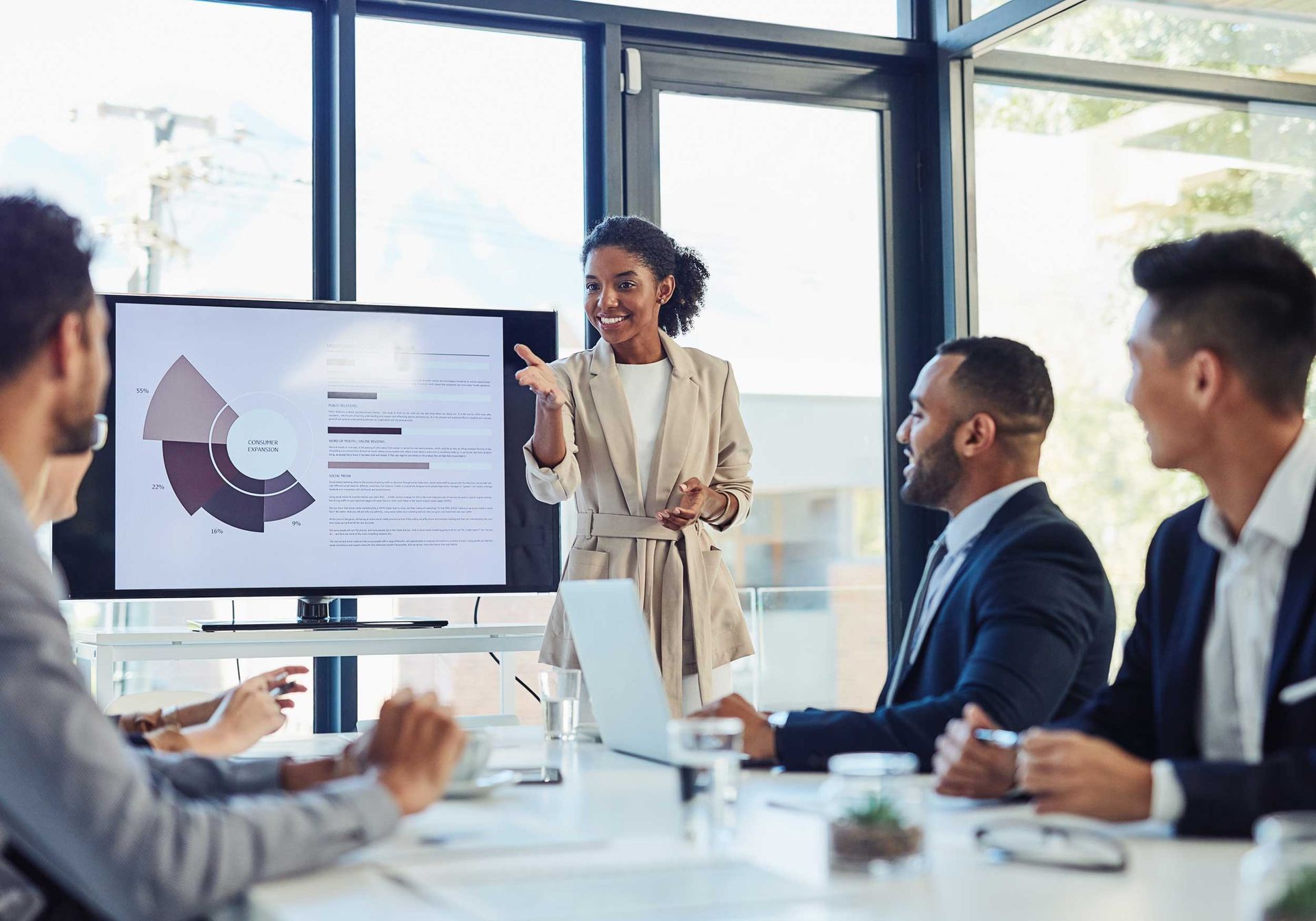 Team meeting in a bright office, presenter showing a chart on a large monitor.