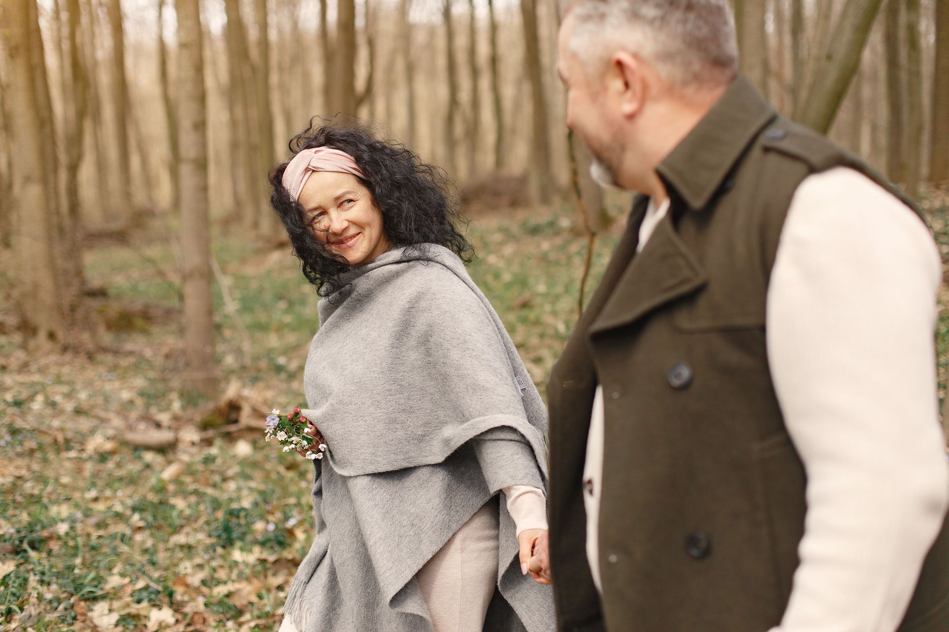 Two people walking in a wooded area, one smiling back over her shoulder.