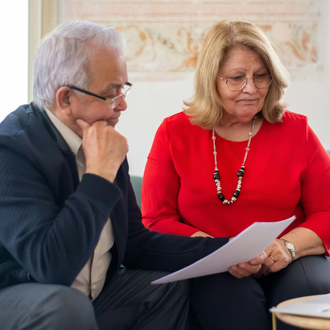 Two people seated indoors reviewing a document, one holding the paper and the other listening attentively.