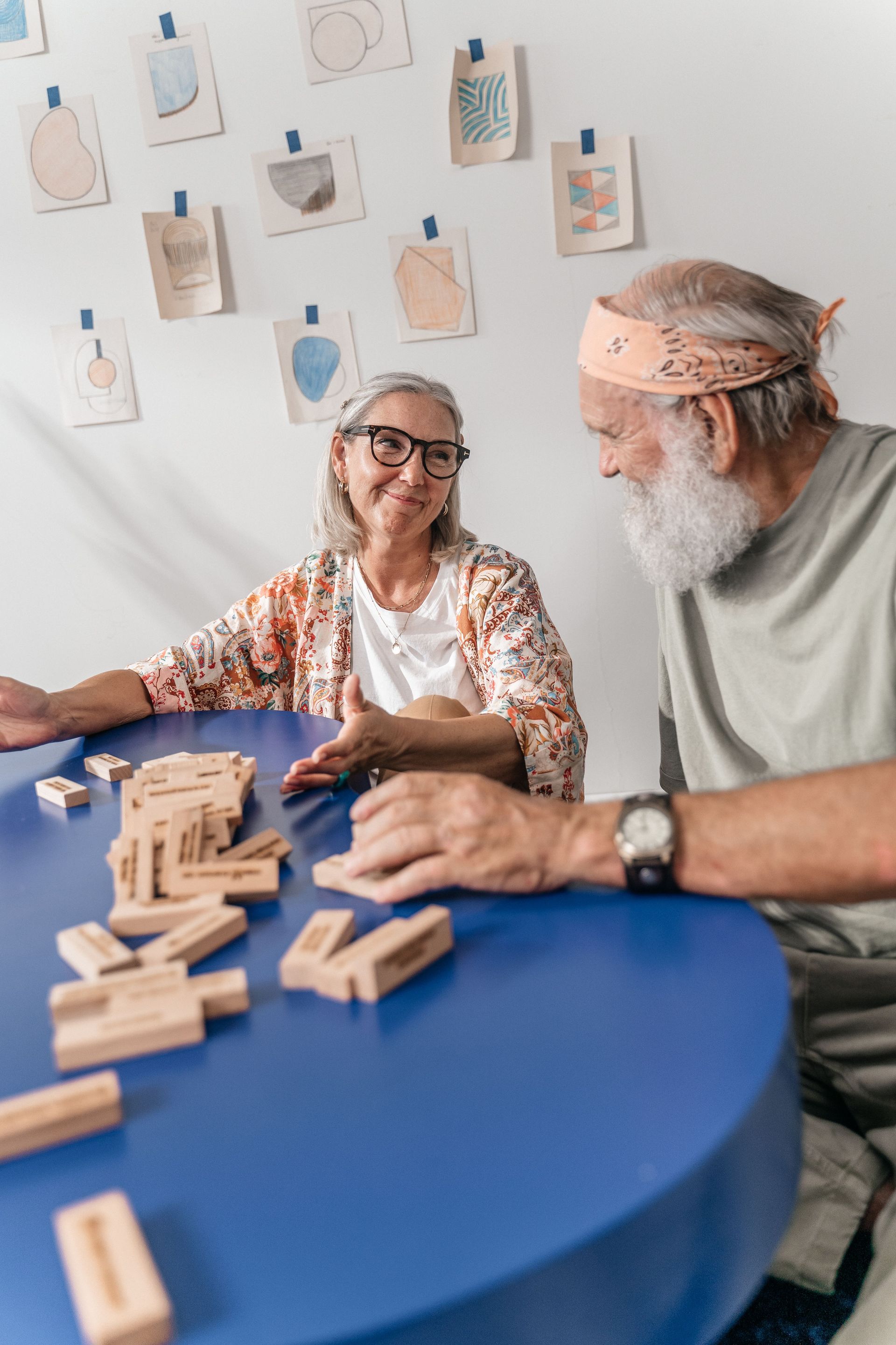 Two people playing wooden blocks at a blue table in a bright room
