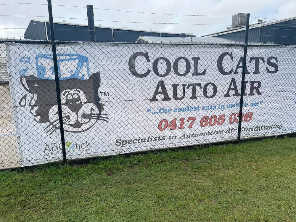 A Sign for Cool Cats Auto Air is Hanging on a Chain Link Fence — Cool Cats Auto Air in Urangan, QLD