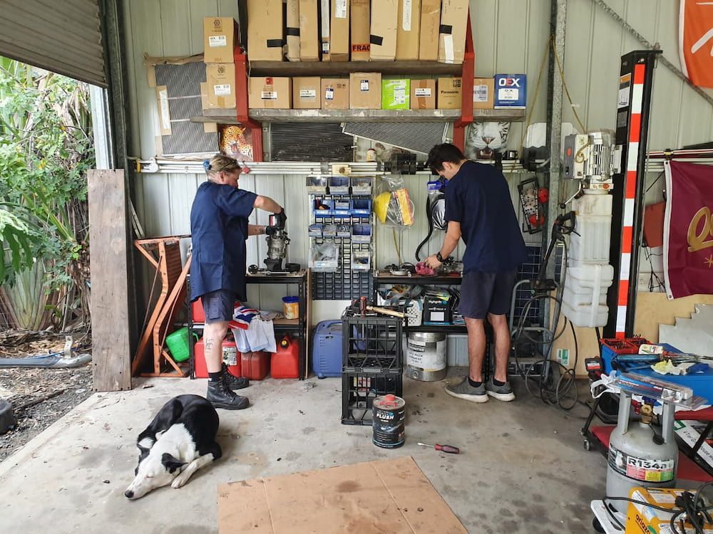 Two Men Are Working in a Garage With a Dog Laying on the Ground — Cool Cats Auto Air in Urangan, QLD