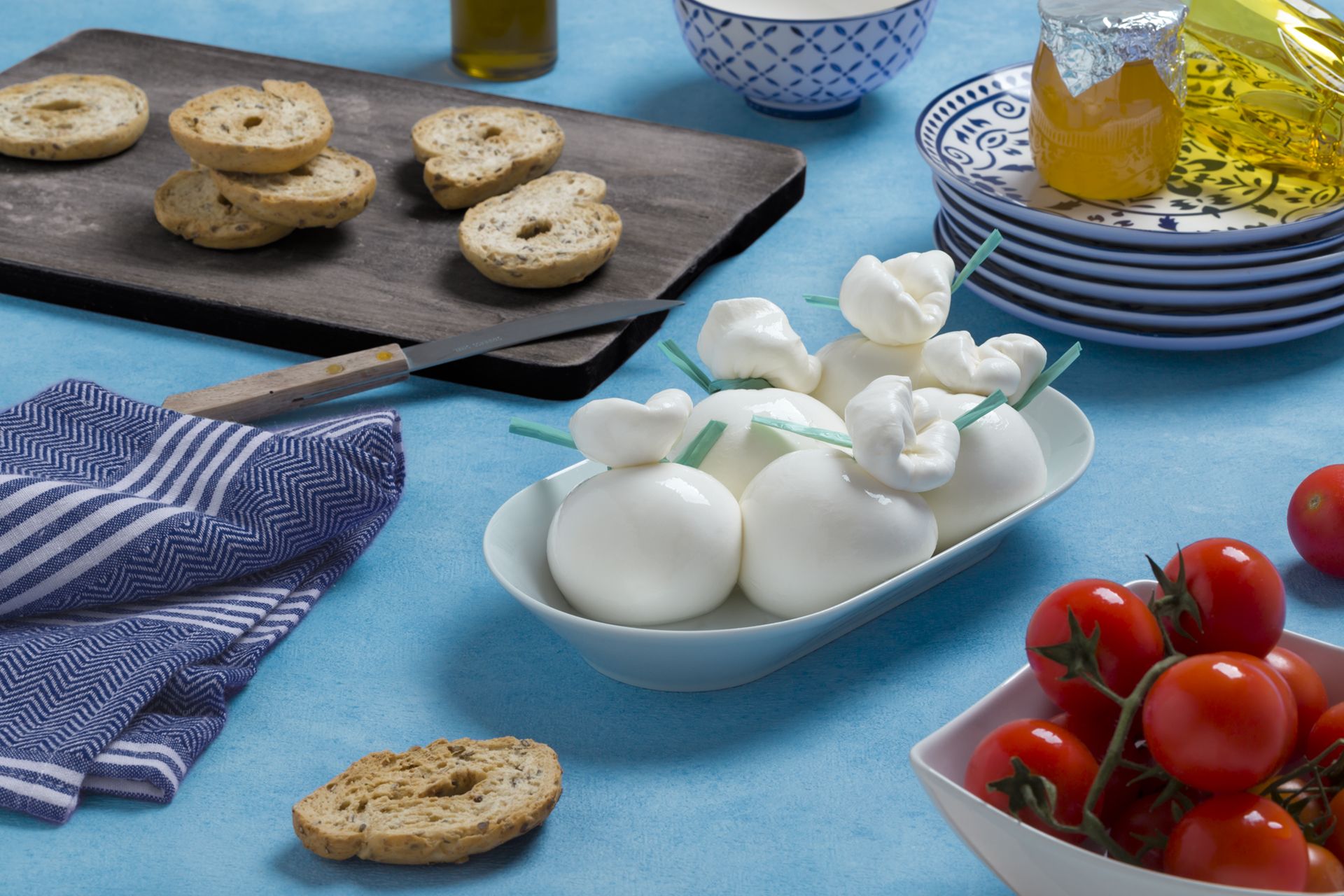 Burrata fresca, pomodori, pane e olio d'oliva su un tavolo blu.