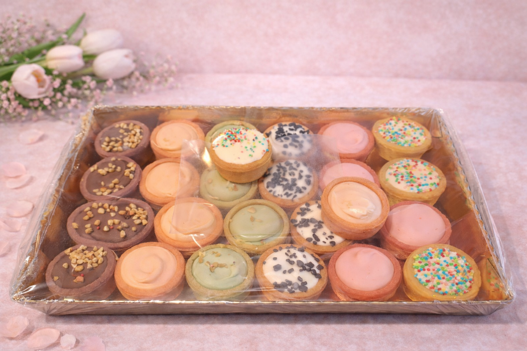 Vassoio di macarons colorati, alcuni con granella, noci e guarnizioni, su uno sfondo rosa.
