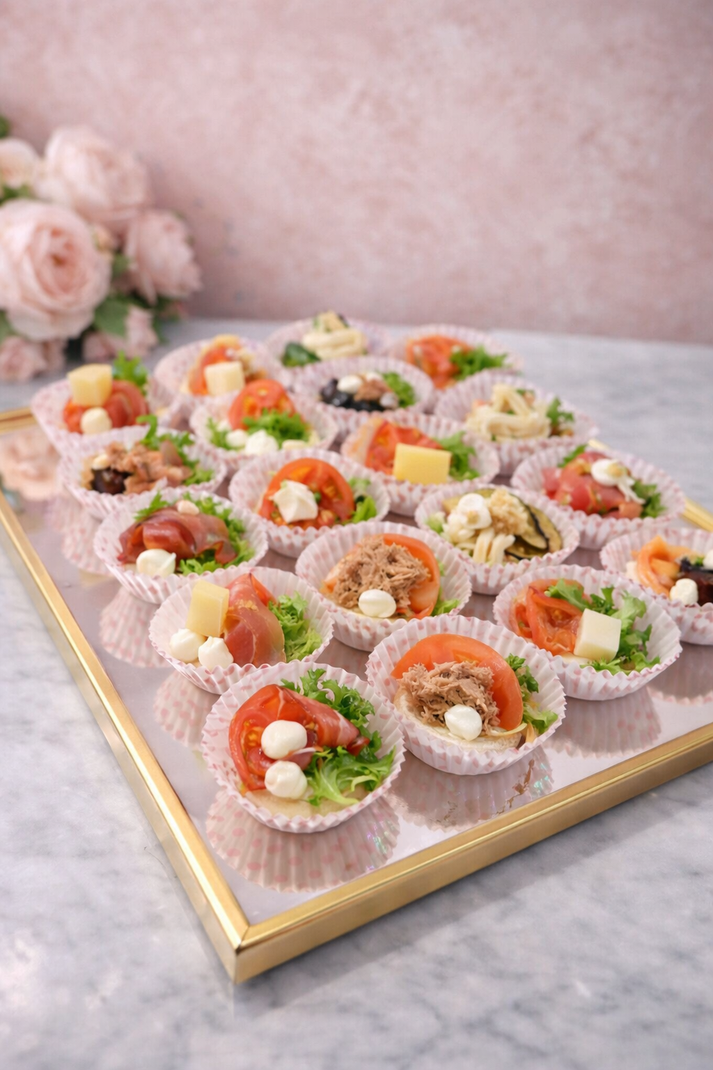 Vassoio di antipasti con mini insalate assortite in bicchieri di carta, disposte su un vassoio con bordo dorato.