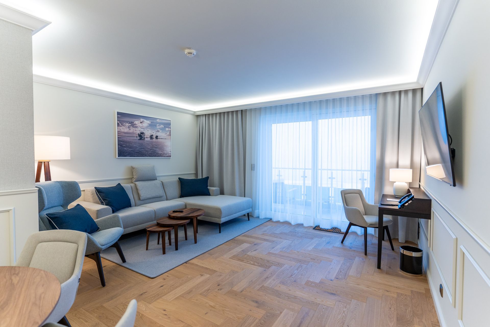 Ein Wohnzimmer mit Couch, Sesseln, Schreibtisch und Fernseher.
